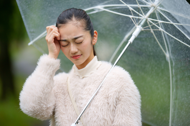 透明な傘を差して頭痛で顔をしかめる女性