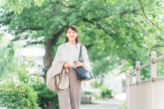 椎間板ヘルニアが改善し新緑の木陰を歩く中年ビジネスウーマン