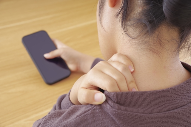 首・肩が痛そうにスマホを操作している女性