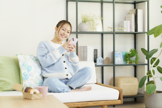 ソファに座ってスマホを手に笑う若い女性