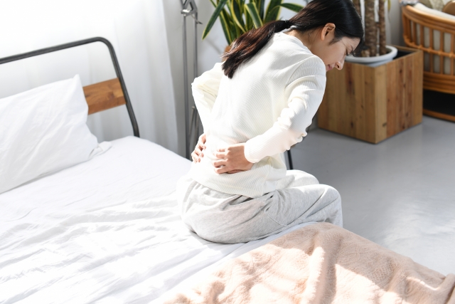 ベッドの上で腰痛や背痛に悩む女性