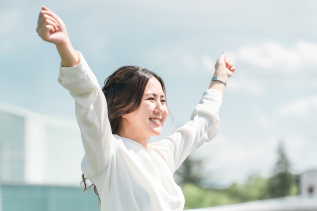 首こりが解消しバンザイをするビジネスウーマン