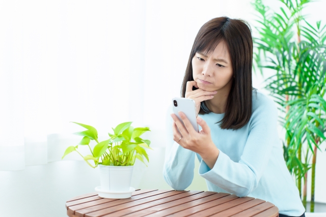 困った表情でスマートフォンを使う女性