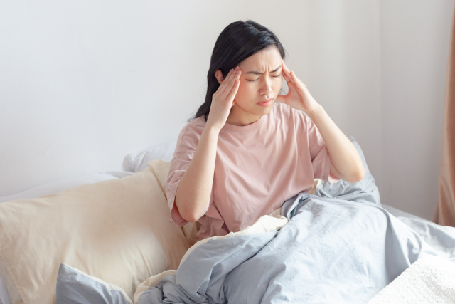 ベッドでこめかみを抑える女性